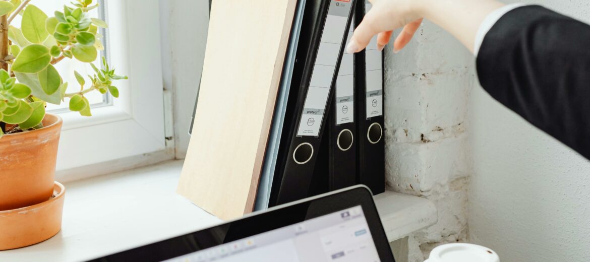 Käsi kurottaa tietokoneen yli nappaamaan kansiota.