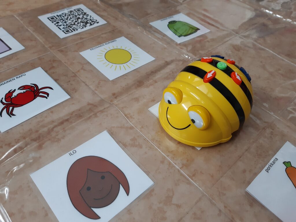 Bee-Bot kirkkaalla muovimatolla, jonka alle on sijoitettu erilaisia kuvakortteja.
