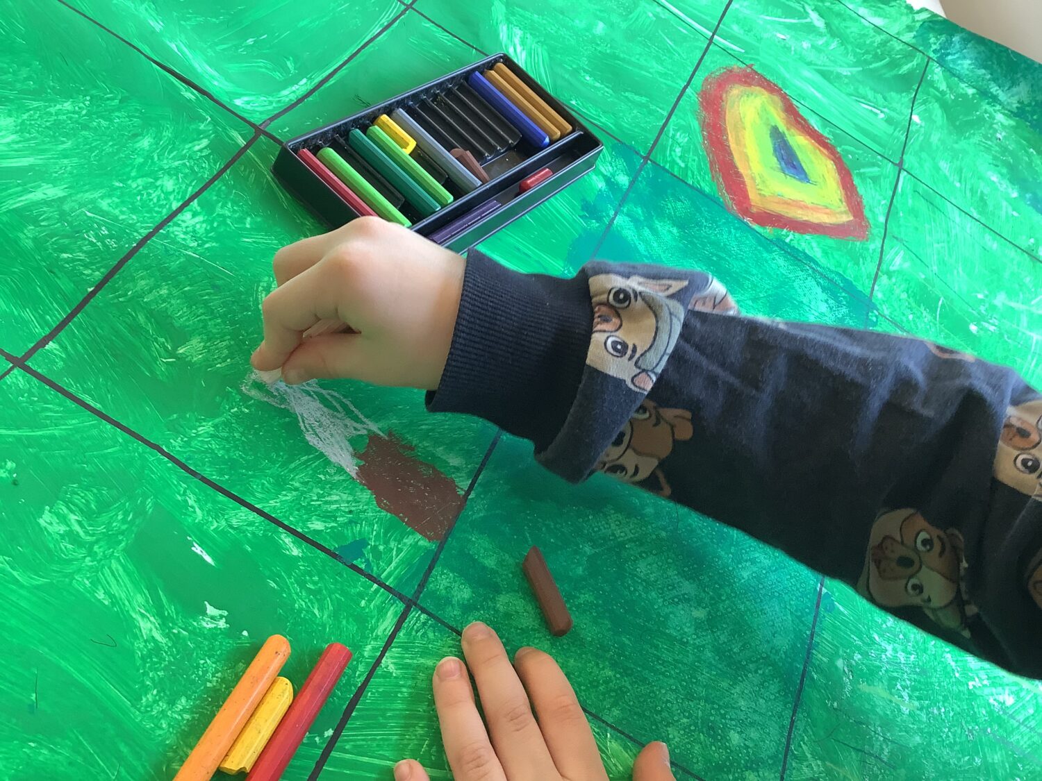 Lapsen käsi piirtää vahaliiduilla vihreään ruudukkoon.