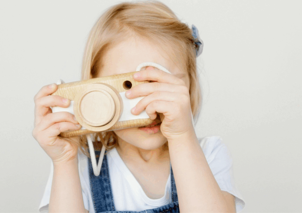 Lapsi, joka leikkii puisella kameralla.